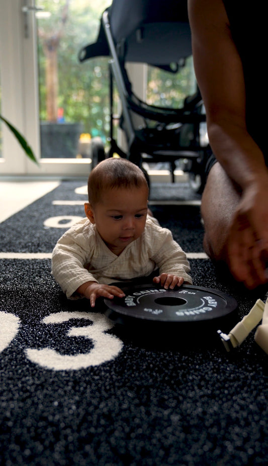 Baby on tummy time grabbing a Baby Gains plate on the black Grass Mat with white numbered markers